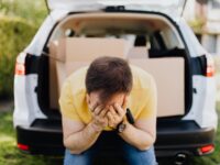 A man holding his head in front of his car full of moving boxes